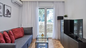 Un salon moderne avec un canapé gris, des coussins rouges, une table basse en verre, un téléviseur à écran plat et une porte-fenêtre coulissante donnant sur un espace extérieur.