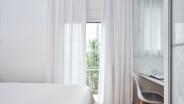 Une chambre à coucher avec un lit, un bureau et une chaise. Il y a une fenêtre avec des rideaux, et de là, on peut admirer la verdure à l’extérieur.