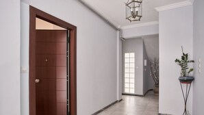 Un couloir avec une porte en bois, une plante en pot et un luminaire suspendu.