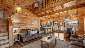 Ein gemütliches Blockhaus-Interieur mit Holzbalkendecke, einem Wohnzimmer mit Sofa und Couchtisch, einer Küchenzeile und einem Esstisch.
