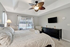 A bedroom with a bed, a ceiling fan, a TV, a dresser, and a window with curtains. - Luxurious Heated Saltwater Pool Home (Cape Coral)