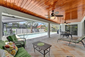 Un patio exterior con piscina, mobiliario de mimbre y un ventilador de techo.