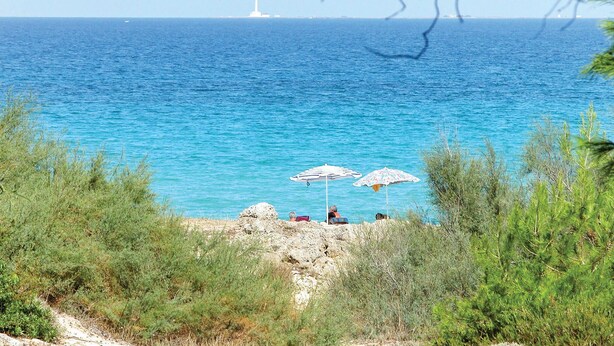 Vista costanera amb dues paraigües de platja, terreny rocos i un far a la distància.