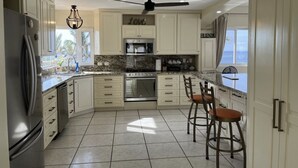 A spacious kitchen with white cabinets, a granite countertop, a built-in oven, and a ceiling fan. - Beautiful Ocean View Home (Cabo San Lucas)