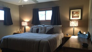 A bedroom with a large bed, two bedside lamps, a nightstand, a framed picture on the wall, and a ceiling fan.