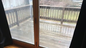 A wooden deck with a metal railing, a sliding glass door, and a wooden floor inside a room.