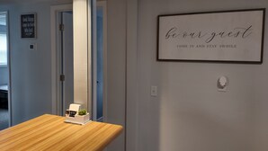 Een kamer met een houten tafel, een bordje in een lijst aan de muur, en een deur naar een andere kamer.