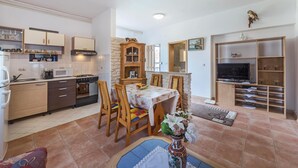 A compact kitchen with a stove, microwave, and cabinets, a dining area with a table and chairs, and a TV in a wooden entertainment unit.