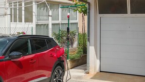 En röd bil står parkerad framför ett hus med en vit garageport, en grön trädgårdsslang och ett stängsel av sammanlänkade metallkedjor.