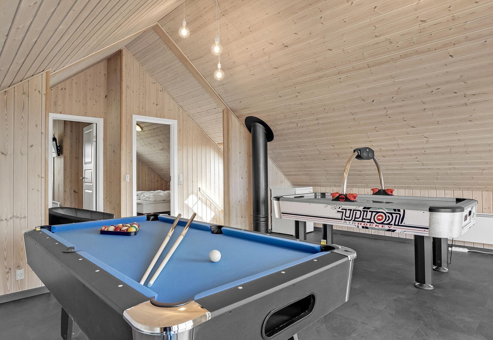 Un tavolo da biliardo con stecche e palle, un tavolo da calcio e un letto in una stanza con pareti in legno e un soffitto spiovente.