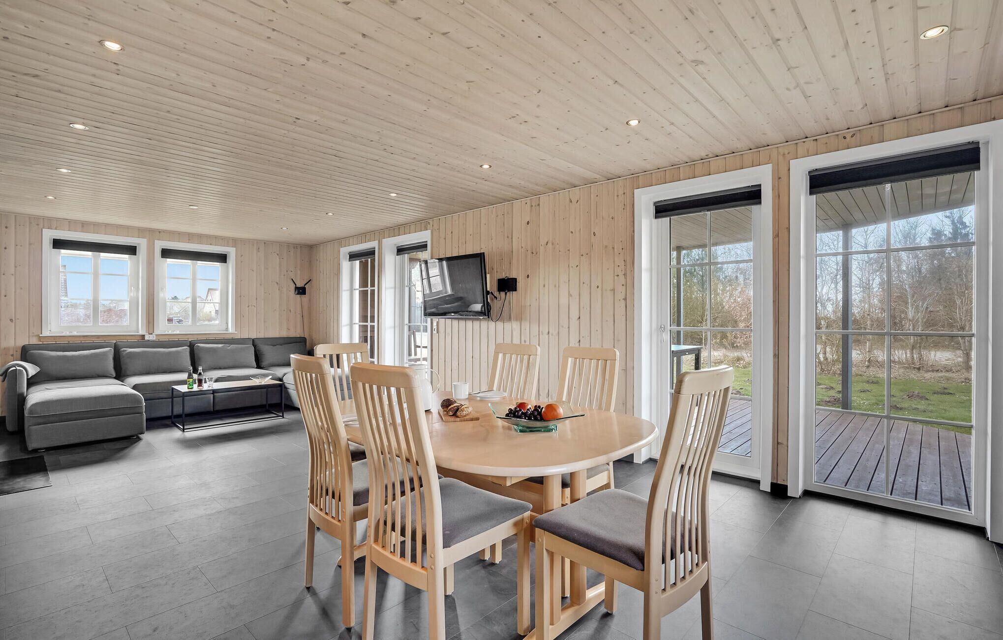 Een modern interieur met een houten plafond, een ronde eettafel met stoelen, een bank en een aan de muur bevestigde televisie.