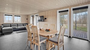 Ein modernes Interieur mit Holzbalkendecke, einem runden Esstisch mit Stühlen, einer Couch und einem an der Wand montierten Fernseher.