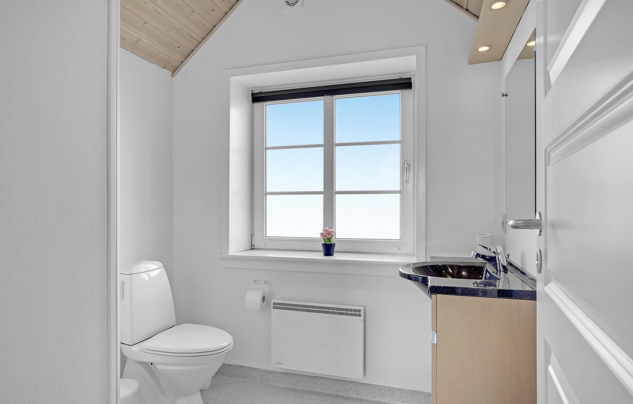 Un baño compacto con inodoro blanco, un ventanal con vistas y un lavamanos con espejo.