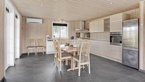 Eine moderne Küche mit Holzvertäfelung, einem Essbereich mit Stühlen, einem Kühlschrank und einer Kaffeemaschine.