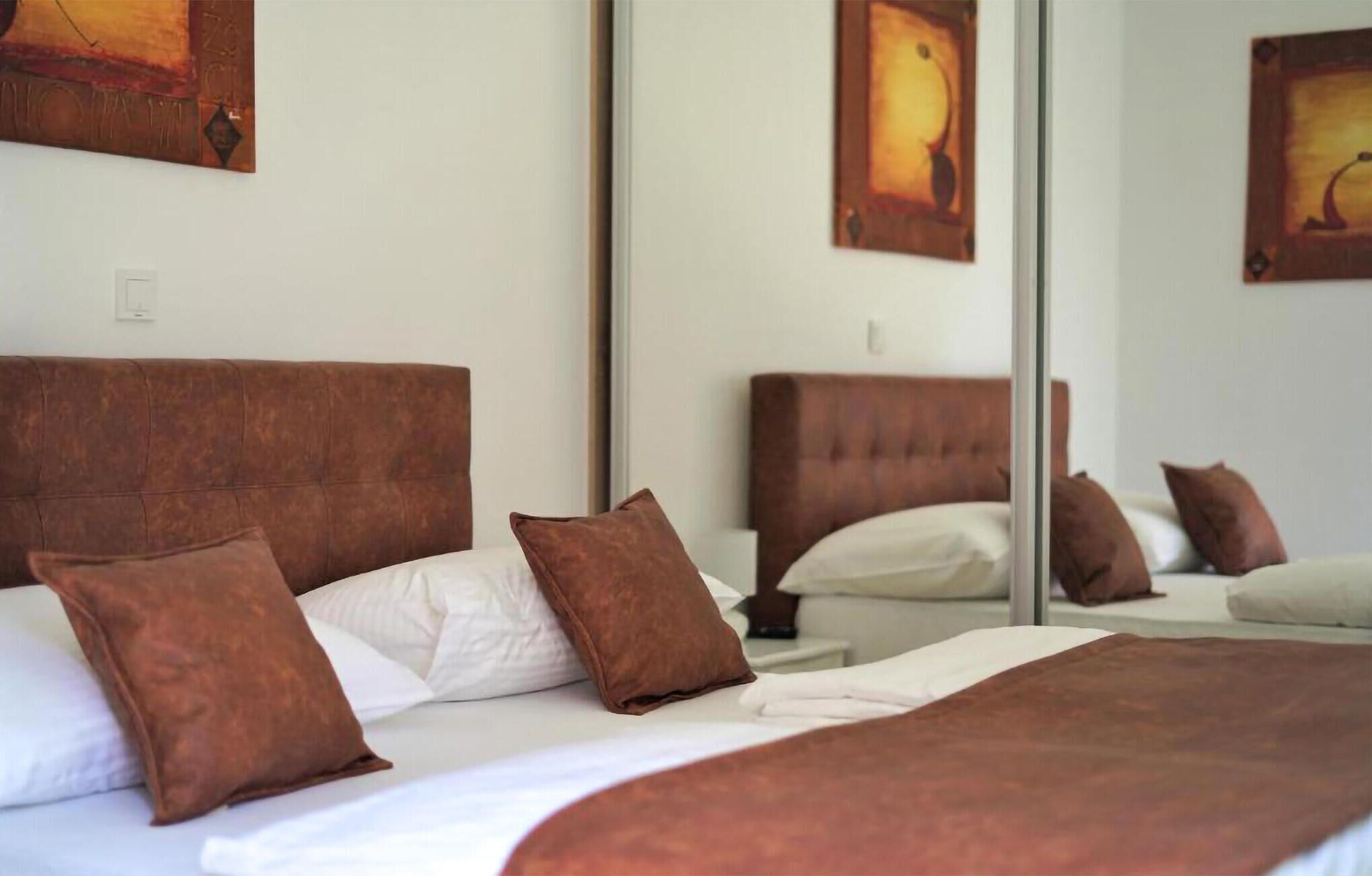 A hotel room with a large bed, brown headboard, white bedding, and a mirror reflecting the room.