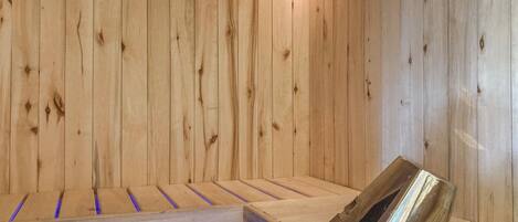 A wooden sauna with benches and a metal bucket.
