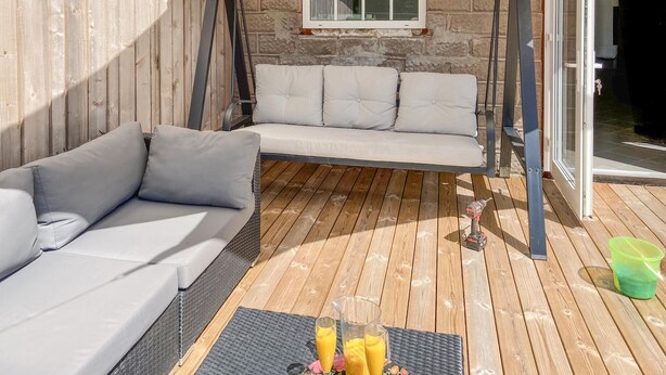 A wooden deck with a sofa and a swing chair, a table with drinks, and a window with a view. - Cozy home in Sollebrunn with sauna (Sollebrunn)