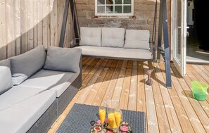 Une terrasse en bois avec un canapé et un fauteuil suspendu, une table avec des boissons et une fenêtre donnant sur un paysage agréable.