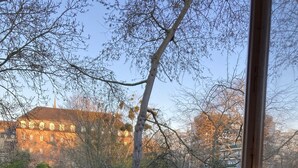 Een balkon met een houten tafel en een klapstoel, met uitzicht op een gebouw met ramen en bomen.