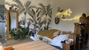 Een slaapkamer met een bed, een houten dressoir, een spiegel en een muur met een tropische plantenmuur.