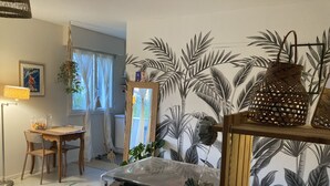 Een kamer met een houten tafel, stoelen, een spiegel en een muur met een tropisch bladpatroon.