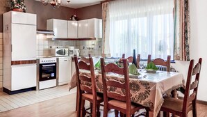 A compact kitchen with modern appliances, a dining area with wooden chairs and a table set for four, and a large window with sheer curtains. - 2 bedroom awesome home in Burg-Reuland (Burg-Reuland)