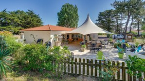 Un espace extérieur abrité, doté de tables et de chaises, entouré de verdure et délimité par une clôture en bois.