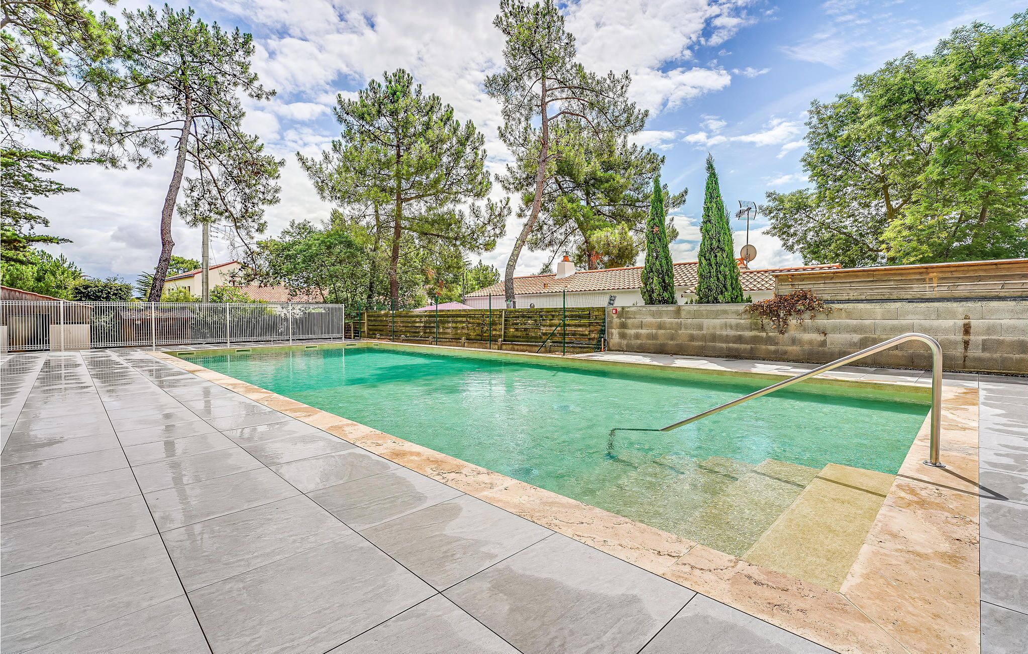 A swimming pool with clear water, surrounded by a tiled deck and a metal fence.