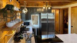A modern kitchen with wooden cabinetry, stainless steel appliances, and a hanging light fixture. - Wildlife Cabin - By Magic Springs, Off-Road Park (Hot Springs)