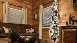 A cozy cabin interior with a wooden interior, a leather sofa, a Christmas tree, and a fireplace. - Wildlife Cabin - By Magic Springs, Off-Road Park (Hot Springs)