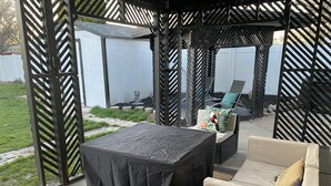 Un espace extérieur abrité avec une table et des chaises, un petit jardin et un bâtiment blanc en arrière-plan.