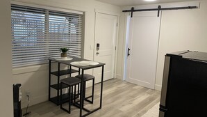 Une petite cuisine avec une fenêtre, un évier, des tabourets, un réfrigérateur et une porte.