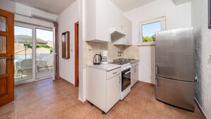 A compact kitchen with white cabinets, a stainless steel refrigerator, a coffee maker, and a window overlooking a green landscape. - Cozy apartment in Barbat na Rabu with WiFi (Barbat na Rabu)