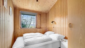 A bedroom with a wooden ceiling, a large window, a bed with white bedding, and a bedside table with a lamp. - Awesome home in Væggerløse with kitchen (Væggerløse)