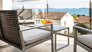 Un balcon avec vue sur la mer, une table garnie de fruits et un fauteuil en osier.