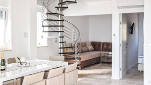 Un salon moderne avec un escalier en colimaçon, un canapé, un coin repas avec une table et une porte donnant sur une autre pièce.