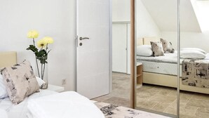Une chambre à coucher avec un lit, une table de chevet ornée d’un vase de fleurs, une armoire et un grand miroir qui reflète la pièce.