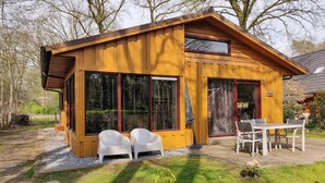 Une cabane en bois dotée de grandes fenêtres, d’une terrasse avec des chaises et d’une enseigne sur laquelle on peut lire « Eikdorp ».
