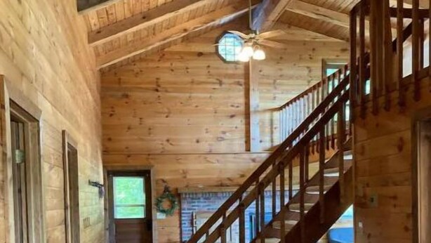 A wooden interior with a staircase leading to a second floor, a ceiling fan, and a brick floor. - Goose Lake Cabin - two lakes to enjoy! (Spooner)
