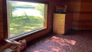 A wooden cabin room with a large window, a small wooden desk, a dresser, and a carpeted floor. - Goose Lake Cabin - two lakes to enjoy! (Spooner)