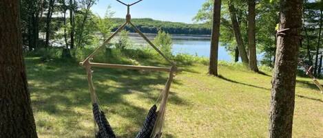 A hammock suspended between trees in a wooded area with a lake in the background.