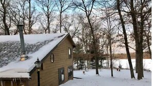A wooden cabin with a chimney, surrounded by snow-covered ground and trees. - Goose Lake Cabin - two lakes to enjoy! (Spooner)