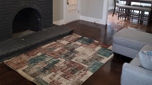 Un salon doté d’une cheminée, d’un téléviseur fixé au-dessus, d’un coin repas avec une table et des chaises, et d’un ventilateur de plafond.