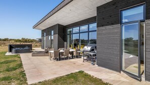 Una casa moderna con ampie finestre, un patio con mobili da esterno e un barbecue.