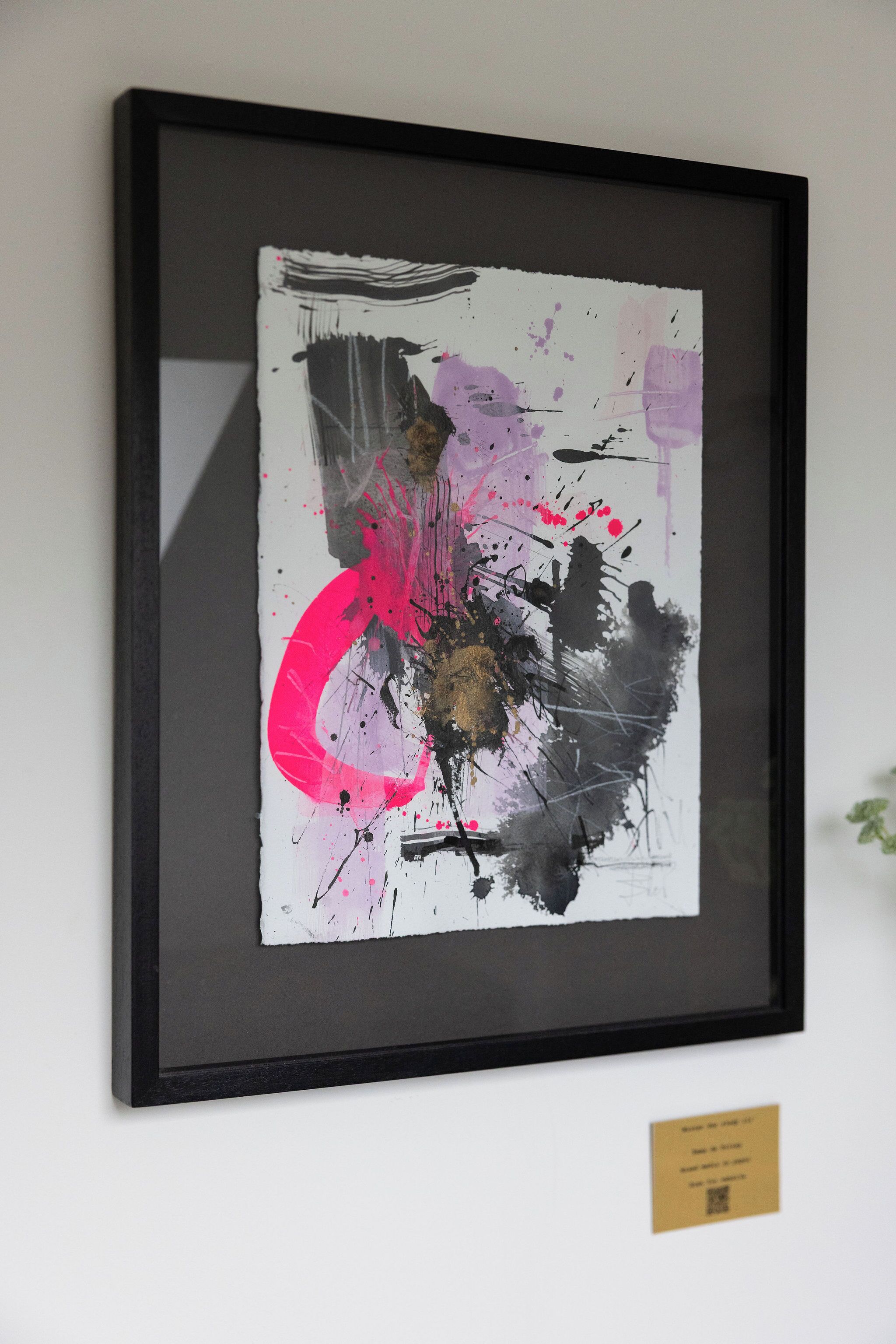 Une peinture abstraite encadrée, avec du texte visible et un code QR, est accrochée à un mur.