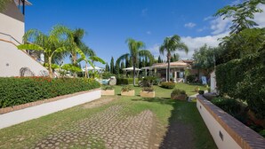 A courtyard with a paved walkway, palm trees, and a pool area. - Lovely apartment in Ricadi with swimming pool (Ricadi)