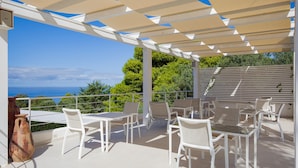 An outdoor patio with white furniture and a view of the sea. - Lovely apartment in Ricadi with swimming pool (Ricadi)