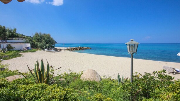 A beach with a clear blue sky, a white building with a tiled roof, and a lamp post. - Lovely apartment in Ricadi with swimming pool (Ricadi)