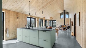 A modern kitchen with a central island, wooden walls, and large windows.