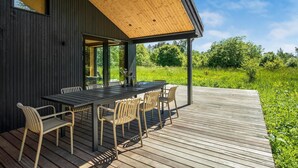A wooden deck with a table and chairs, overlooking a grassy area.